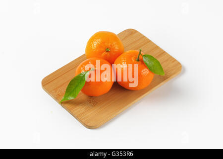Tre i tangerini con foglie sul tagliere di legno Foto Stock