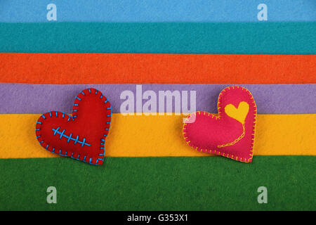Artigianato e arte, due cucito a mano giocattolo Cuori rosa e rosso sul feltro colorato sfondo strisce Foto Stock