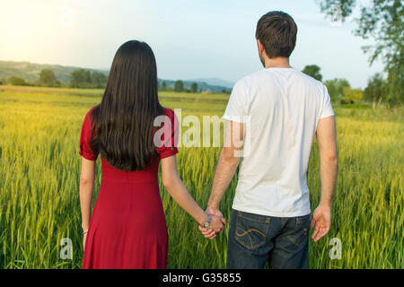 Giovane tenendo le mani in un campo di grano rivolta verso il tramonto Foto Stock