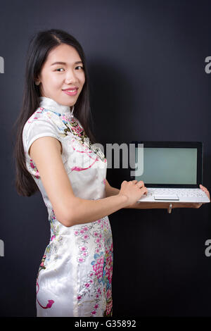 Giovane donna asiatica in possesso di un computer portatile di indossare abiti cinesi Foto Stock