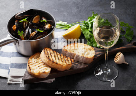 Le cozze in pentola di rame, crostini di pane e vino bianco sul tavolo di pietra. Focus sul vetro del vino Foto Stock