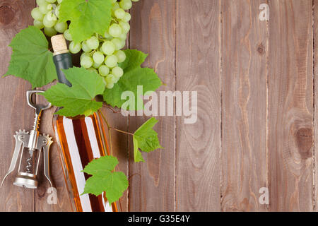 Grappolo di uva, vino bianco bottiglia e cavatappi sul tavolo di legno con uno sfondo con spazio di copia Foto Stock