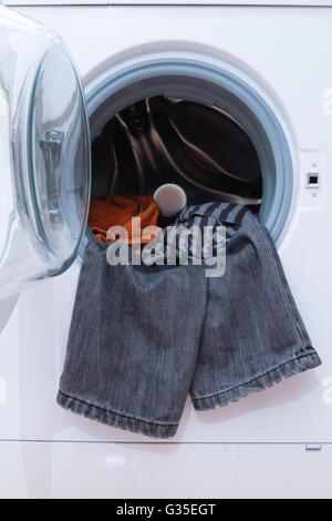 Una chiusura di una macchina di lavaggio caricata con i vestiti. Elettrodomestico. Foto Stock