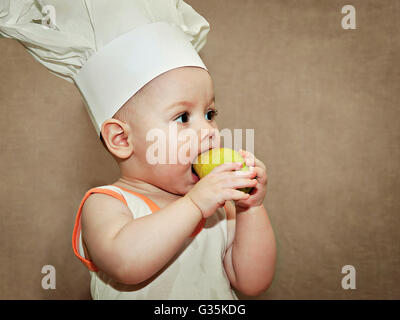 Piccolo bambino in un chef hat mangiare una pera Foto Stock