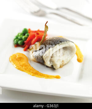 Filetto di branzino su una piastra con la salsa di peperoni e piselli verdi. Foto Stock