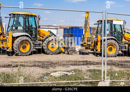 Vista su alcuni escavatori attraverso un filo di recinzione, parcheggiato al sito in costruzione. Foto Stock