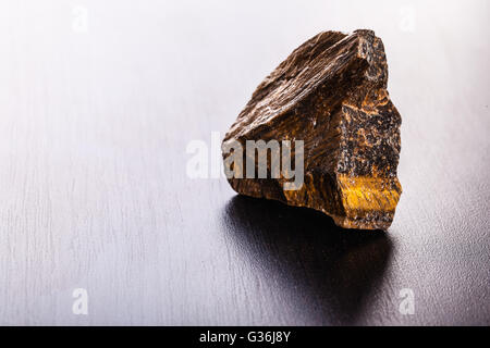 Immagine ravvicinata di un frammento di occhio di tigre minerale su di una superficie scura Foto Stock