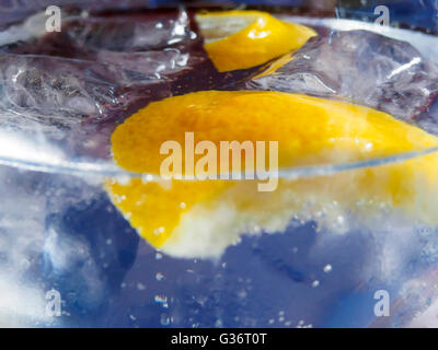 Primo piano di vetro contenente il gorgogliamento di liquido trasparente e le fette di limone e cubetti di ghiaccio Foto Stock