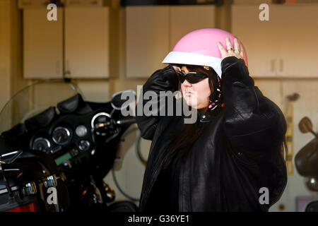 Una ragazza si prepara per una corsa su una motocicletta come lei si mette sul suo casco rosa. Foto Stock