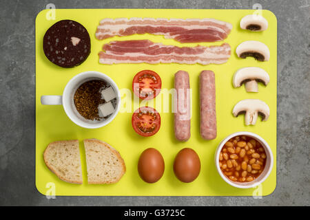 Colpo di overhead di selezione di cibi per la prima colazione inglese su un giallo tappetino da pranzo prevista su un livello di grigio ardesia superficie. Foto Stock