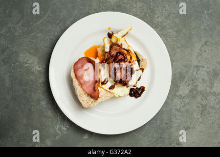 Sovraccarico di uova e pancetta sul rotolo servita su un bianco piastra rotonda Foto Stock