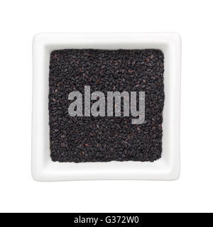 Di semi di sesamo nero in un recipiente quadrato isolato su sfondo bianco Foto Stock