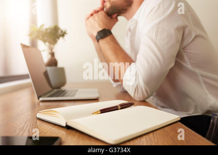 Immagine di agenda elettronica personale sulla tavola con imprenditore seduto in background. Diario con penna sul tavolo con uomo che lavora presso la BAC Foto Stock