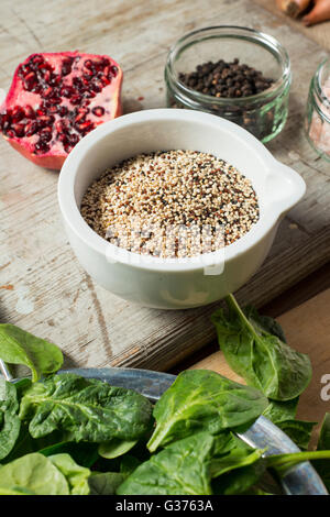 La quinoa in bianco ciotola da una fetta di melograno, grani di pepe, e spinaci Foto Stock