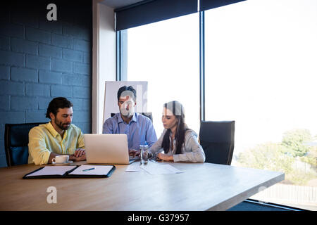 I collaboratori di lavorare intorno a un tavolo con un computer portatile Foto Stock