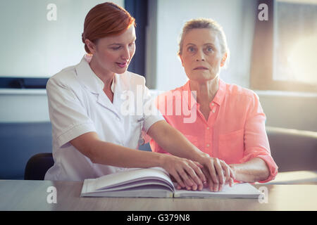 Femmina aiutando infermiere paziente nella lettura del libro in braille Foto Stock