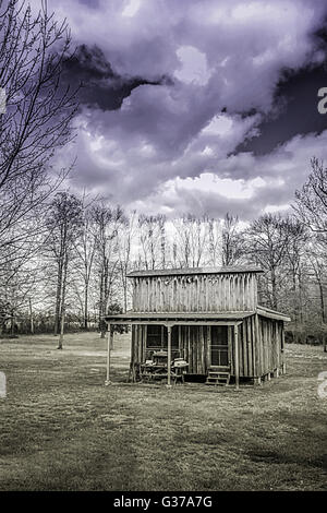 Un rustico di cabina in legno in stile vintage general store si siede in una radura con boschi e drammatica overhead di nuvole Foto Stock