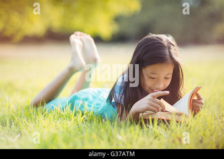 Sorridente ragazza distesa su erba e libro di lettura in posizione di parcheggio Foto Stock