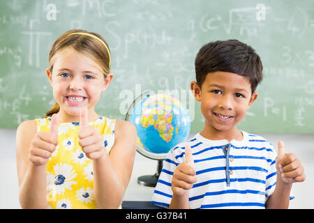 Ritratto di sorridere a scuola i bambini che mostra i pollici fino in aula Foto Stock