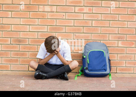 Triste schoolboy seduto da solo in corridoio Foto Stock