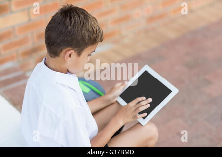 Scolaro seduto in corridoio e con tavoletta digitale Foto Stock