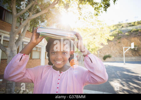 Schoolgirl trasporto di libri sul suo capo Foto Stock