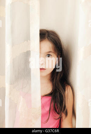 Bambina si nasconde dietro una cortina,guardando la fotocamera Foto Stock