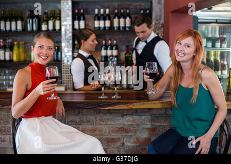 Ritratto di donna felice tenendo un vino rosso di vetro al bancone bar Foto Stock