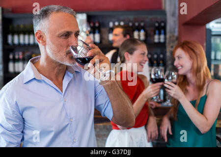 Uomo di bere il vino rosso mentre due amici tostare i bicchieri in background Foto Stock