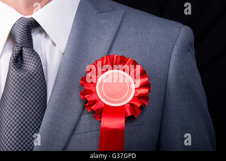 Testa e spalle vista del candidato alle elezioni che indossa un red rosette, contro uno sfondo nero. Foto Stock
