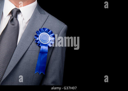 Testa e spalle vista del candidato alle elezioni che indossa una rosetta blu, contro uno sfondo nero. Foto Stock