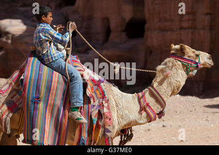 Un giovane beduino a cavallo di un dromedario a Petra, noto anche come "Rose City", Giordania, Medio Oriente. Foto Stock