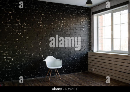 Bianco moderno sedia nero e sfondo mattone. In stile loft. Sedia minima e la camera. Eleganza sedia. Foto Stock