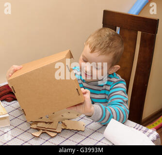 Ragazzo seduto a un tavolo con una scatola di cartone in cui risiede un costruttore di legno Foto Stock