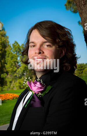 Outdoor ritratto di uno sposo per il suo giorno di nozze. Egli si erge, sorridente alla fotocamera con una rosa boutonnière, stoppia, orecchini, un Foto Stock