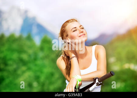 Ritratto di un felice soddisfatta la ragazza con gli occhi chiusi godendo della luce del sole nelle montagne Alpine, viaggiando su una bicicletta Foto Stock