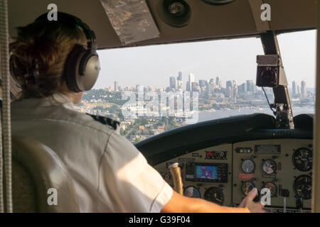 Pilota femmina di float plane provenienti per atterrare sul Lago Union, Seattle con lo skyline della città vista attraverso il finestrino della cabina di pilotaggio. Foto Stock