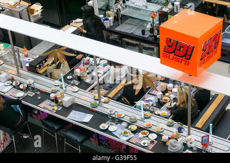 Persone mangiare il cibo Giapponese presso una filiale di Yo! Sushi a Bromley con ciotole di cibo passando sul nastro trasportatore. Foto Stock