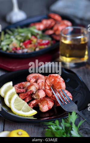 Grigliata di gamberi con limone, verdure e birra. Rustico, low key e bokeh di fondo. Foto Stock