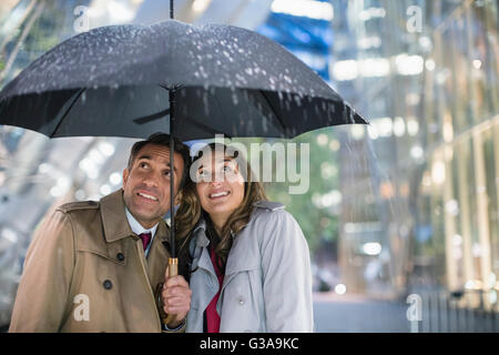 Imprenditore e imprenditrice guardando la pioggia sotto ombrellone Foto Stock