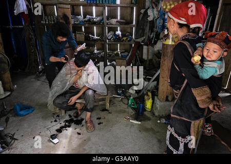 Un Rosso Dao donna e bambino guarda un giovane uomo ha il suo taglio di capelli nel villaggio di Ban Khoang, Sapa, Lao Cai Provincia, Vietnam Foto Stock