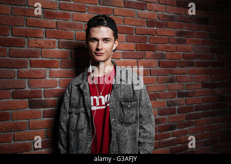 Giovane uomo con gli auricolari per ascoltare musica rosso contro un muro di mattoni Foto Stock