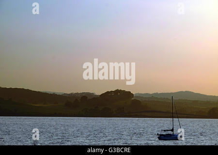 Tramonto sul fiume Exe, con una sola imbarcazione a vela in silhouette Foto Stock