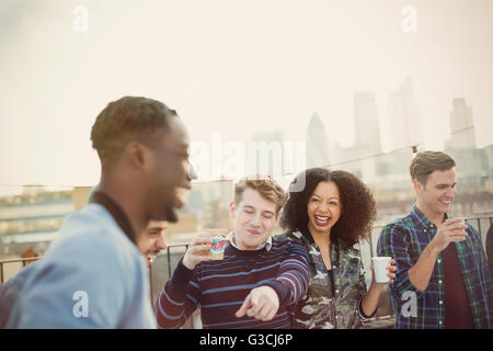 Giovani amici adulti bere e ridere del partito sul tetto Foto Stock