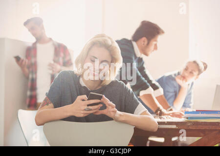 Sorridente giovane imprenditrice texting con il cellulare in ufficio Foto Stock