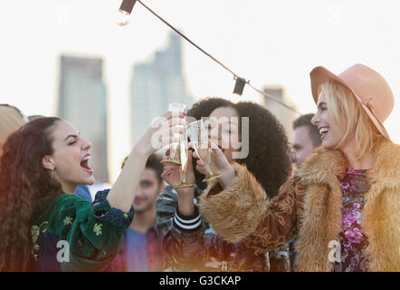 Entusiasti delle giovani donne di tostatura bicchieri di champagne al partito sul tetto Foto Stock