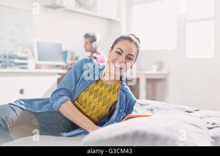 Ritratto sorridente giovane donna adulta la lettura sul letto Foto Stock