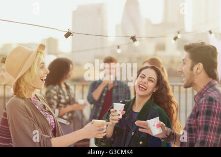 Giovani amici adulti ridere e bere alla festa sul tetto Foto Stock