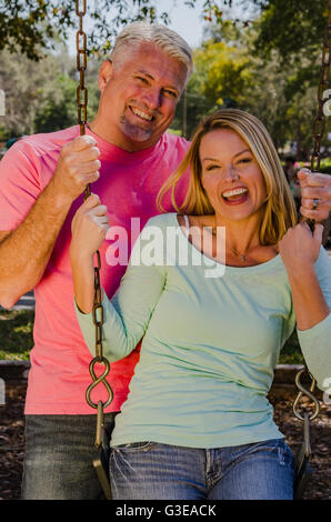Uomo maturo spingendo la sua giovane moglie su uno swing Foto Stock