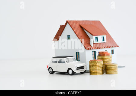 Auto e modello di casa con la pila di monete isolati su sfondo bianco Foto Stock